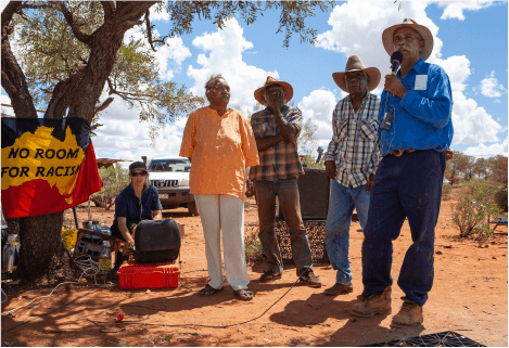 Banjo and other senior men perform ceremonial song at the opening of Protest House.